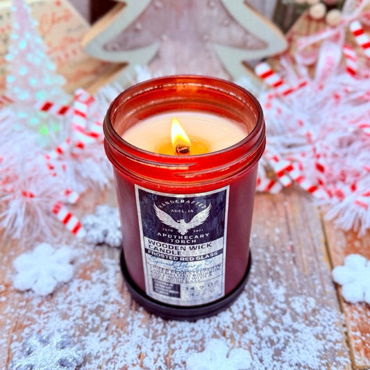 Candle in a red jar with a label on a wooden surface with decorative elements.